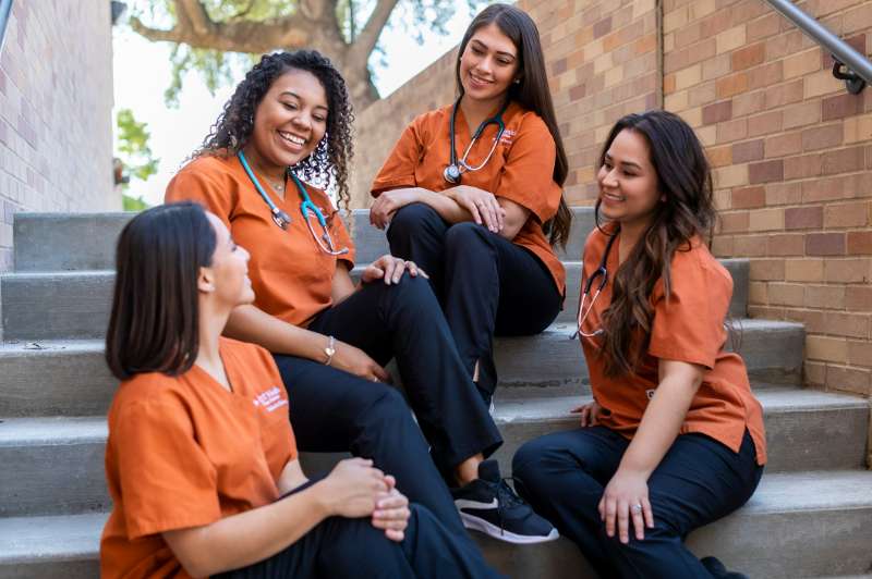 Group of diverse female UT health School of Nursing students sitting on steps conversing with each other